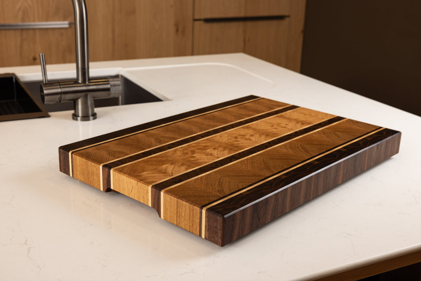 Planche à découper en bois de bout modèle Ravel, en chêne, noyer et érable, posée sur un plan de travail dans une cuisine moderne. Fabrication artisanale française en bois