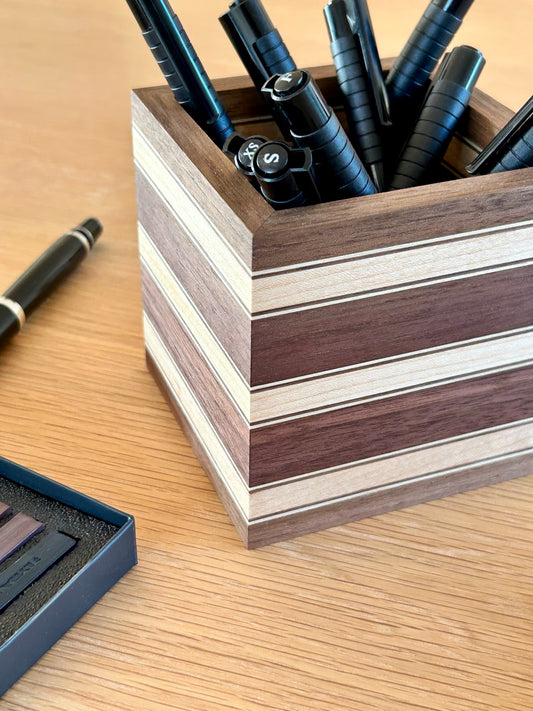 Pot à crayons Debussy en noyer avec des bandes fines en érable, présenté avec des feutres et un stylo plume