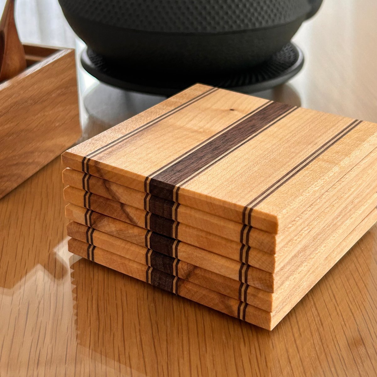 Ensemble de sous-verres en bois fait main, érable, noyer, présenté avec une théière pour illustrer leur usage quotidien.