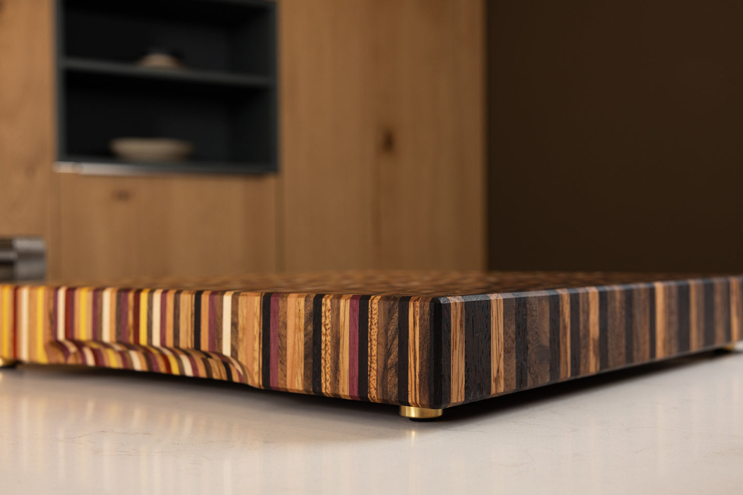 Vue de coté et détail sur les 11 essences et le pied en laiton d'une planche à découper artisanale de luxe fabriquée en France.