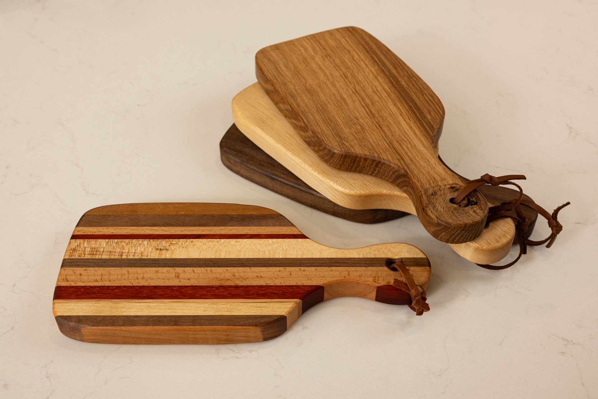 Collection de mini planches à découper Piccolo en bois massif, vue d’ensemble mettant en valeur les essences nobles érable, chêne français et noyer américain, avec lanières en cuir, fabrication artisanale Made in France.