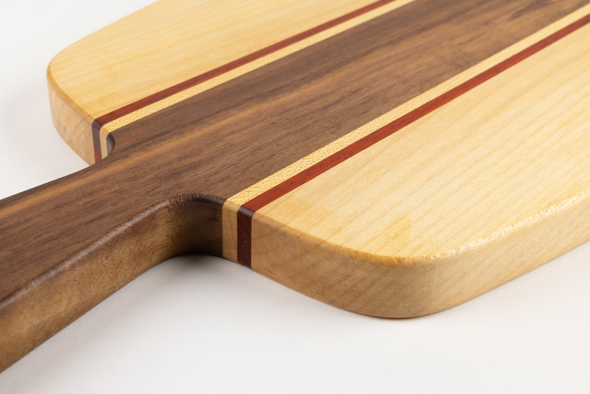 Gros plan sur l’assemblage des essences de bois de la planche apéro : poignée en noyer, filets de padouk et érable, avec finition huilée.