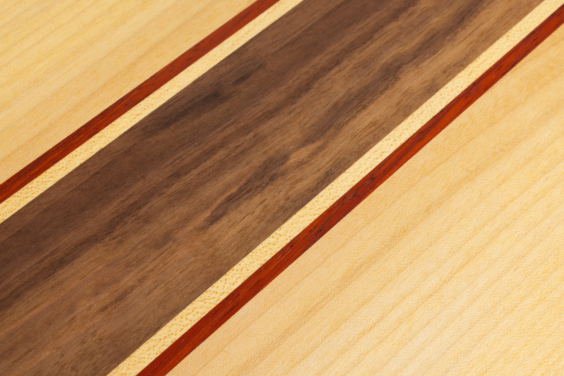 Gros plan sur les essences de bois utilisées pour une planche apéro : noyer, érable et padouk, avec finition huilée mettant en valeur le veinage.