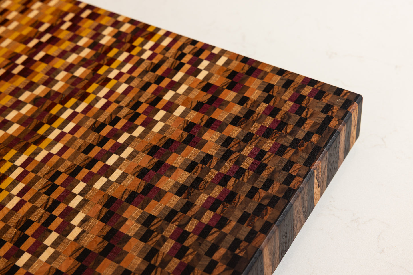 Détail sur le motif en dégradé réalisé avec 11 essences de bois sur une planche à découper artisanale haut de gamme en bois de bout, fabriqué en France.