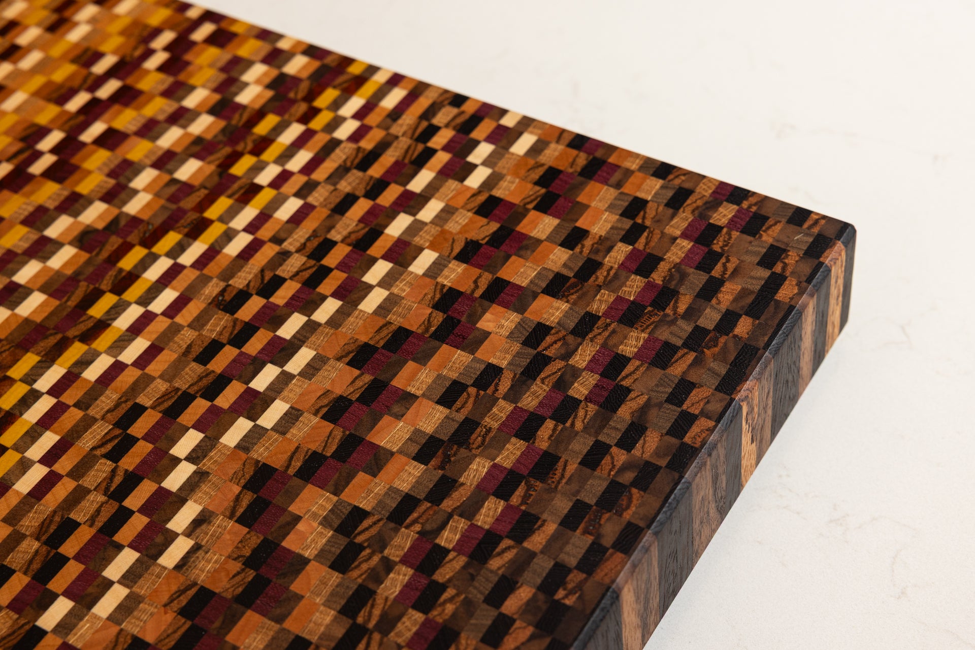 Détail sur le motif en dégradé réalisé avec 11 essences de bois sur une planche à découper artisanale haut de gamme en bois de bout, fabriqué en France.