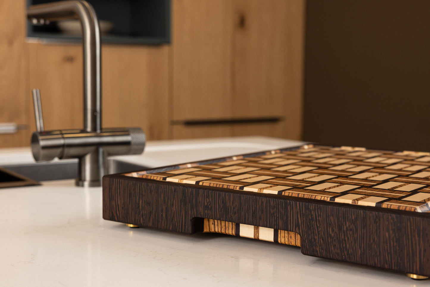Planche à découper en bois de bout fabriquée en France, en zebrano, noyer et érable, trois bois précieux. Pièce artisanale haut de gamme posée sur un plan de travail dans une cuisine moderne