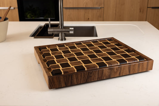 Planche à découper en bois de bout modèle Berlioz, en wengé, noyer et érable, posée sur un plan de travail dans une cuisine moderne. Fabrication artisanale française haut de gamme en bois noble et au design graphique