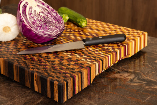 Vue d'une planche à découper artisanale haut de gamme 11 essences en situation avec légumes et couteau de chef.