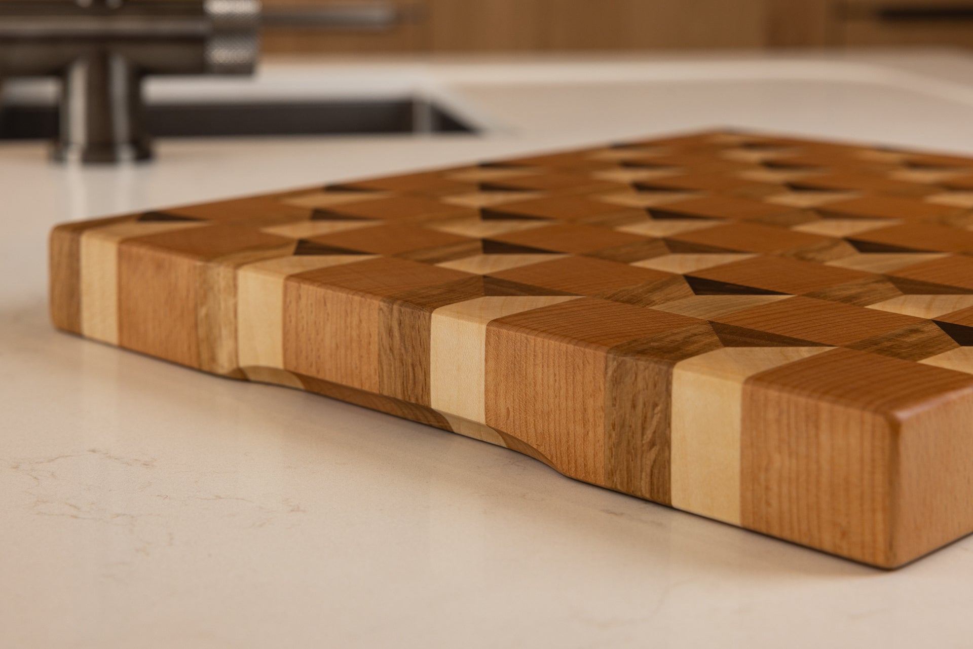 Vue du coin de la planche à découper Cube, bords arrondis et lustrés, design cubique trompe-l’œil en bois noble multi-essences, posée dans une cuisine moderne en chêne.