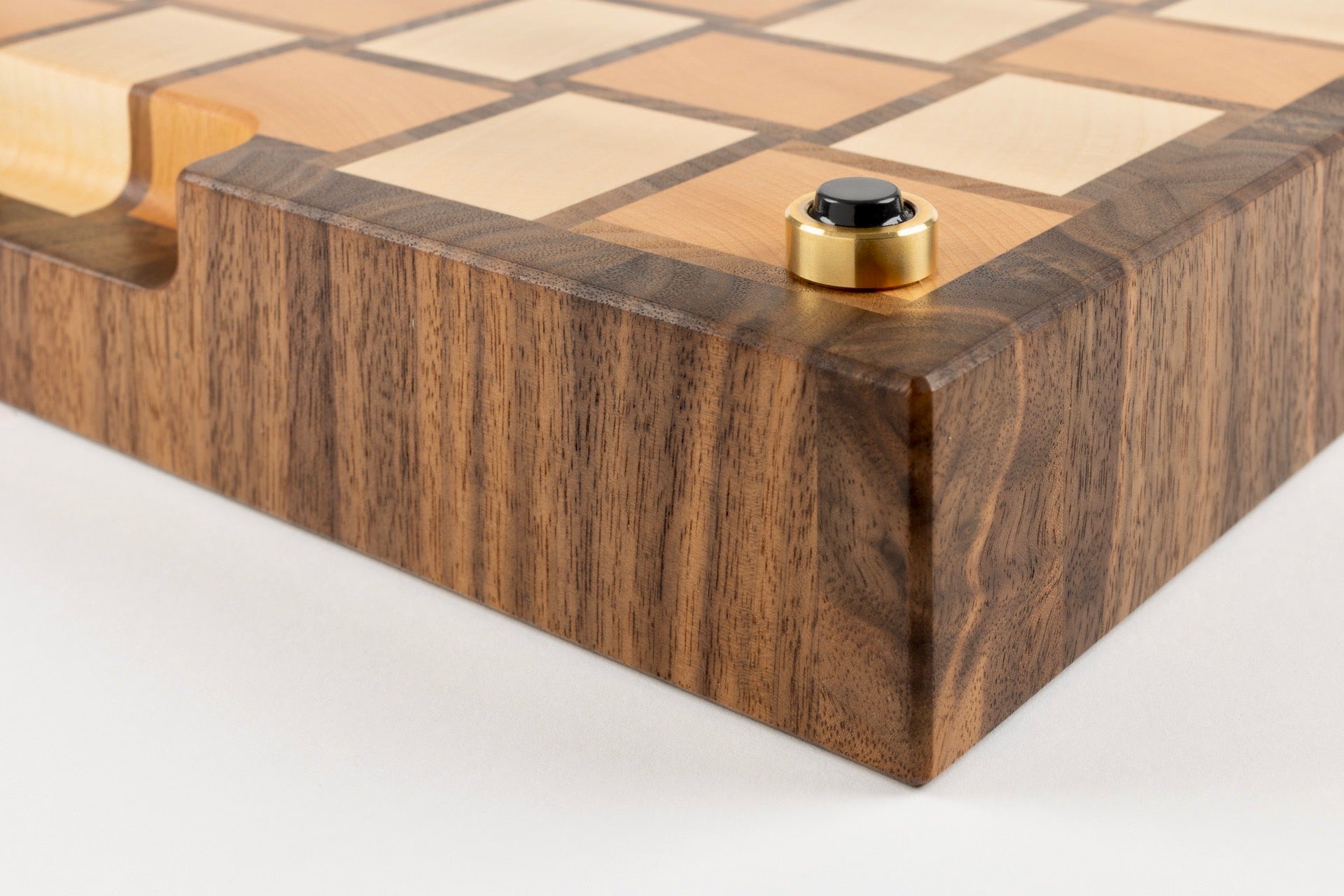 Gros plan sur le coin de la planche à découper Berlioz, motif damier tissé en érable, noyer américain et hêtre, détail du pied en laiton massif fabriqué en France avec patin antidérapant haut de gamme.