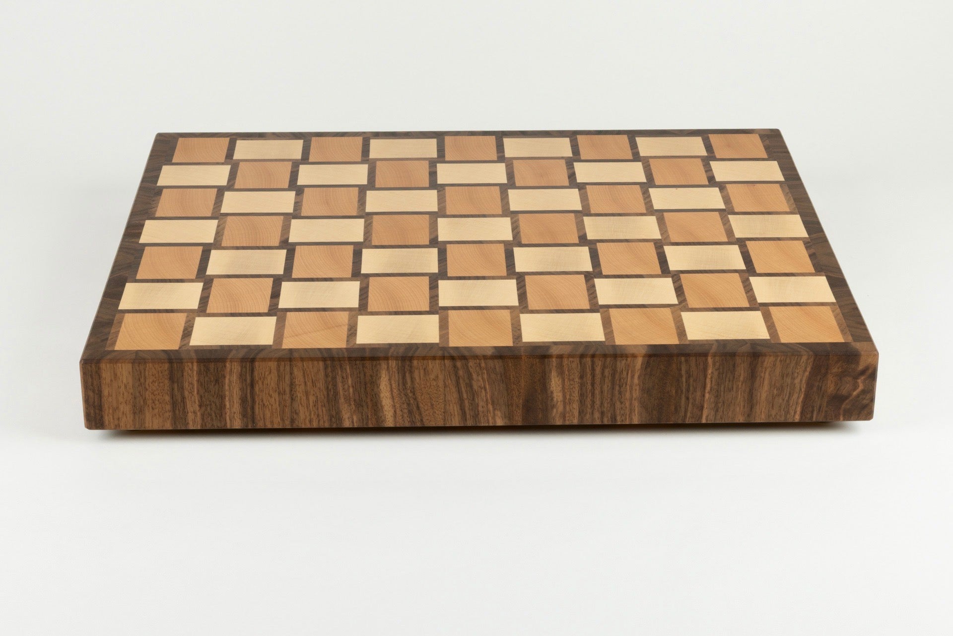 Vue de face de la planche à découper Berlioz, avec bordure élégante et son motif damier tissé en bois de bout, réalisée en érable, noyer américain et hêtre, pièce artisanale française haut de gamme.