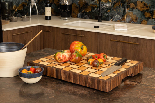 Planche à découper de luxe Berlioz Made in France, en bois de bout avec motif damier tissé élégant, en situation dans une cuisine haut de gamme avec plan de travail en granit, légumes frais et couteau de chef.
