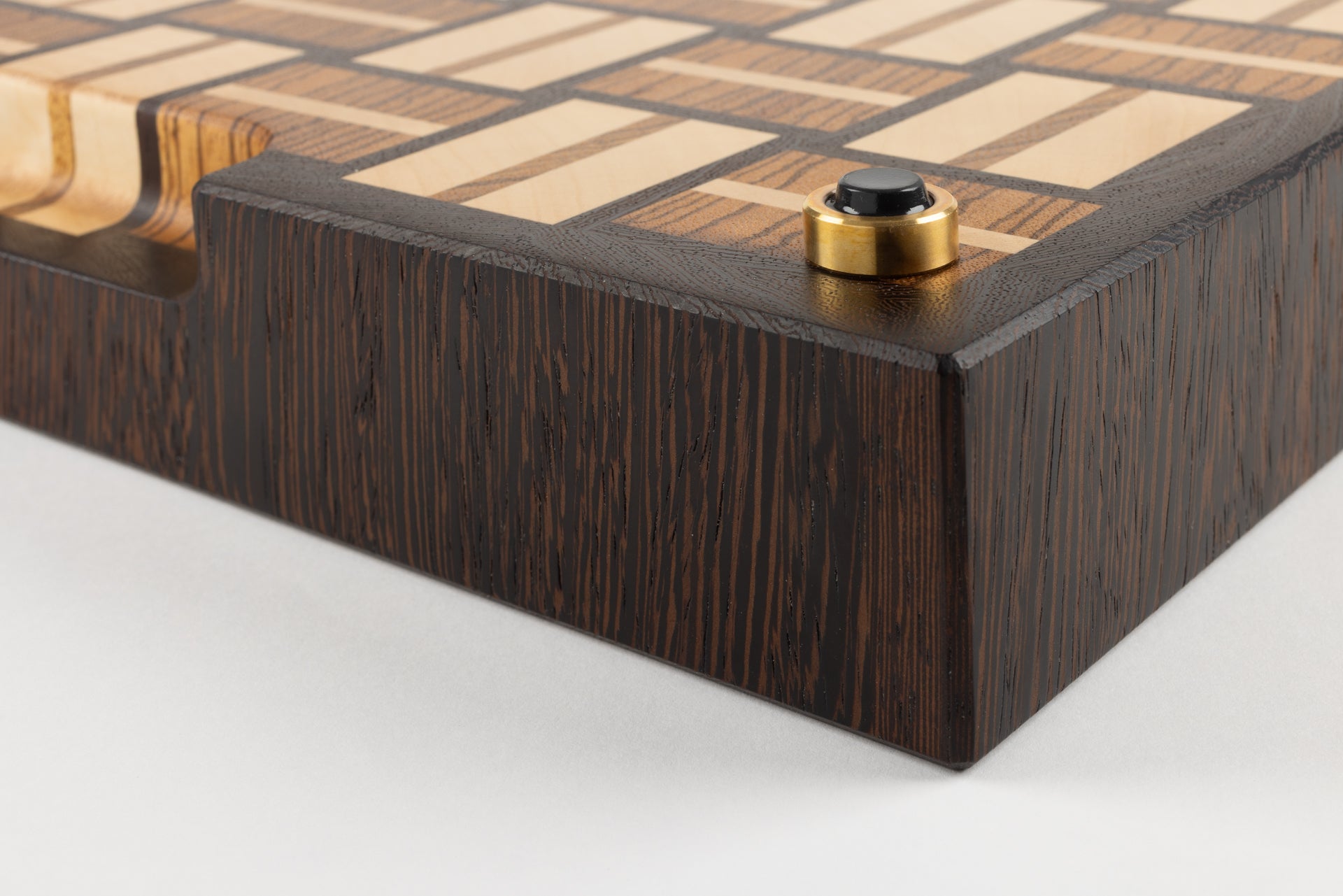 Planche à découper en bois de bout de luxe Berlioz, gros plan sur le coin et le pied en laiton massif fabriqué en France, patin antidérapant de qualité, motif damier tissé en wengé, zebrano et érable, fabrication artisanale haut de gamme.