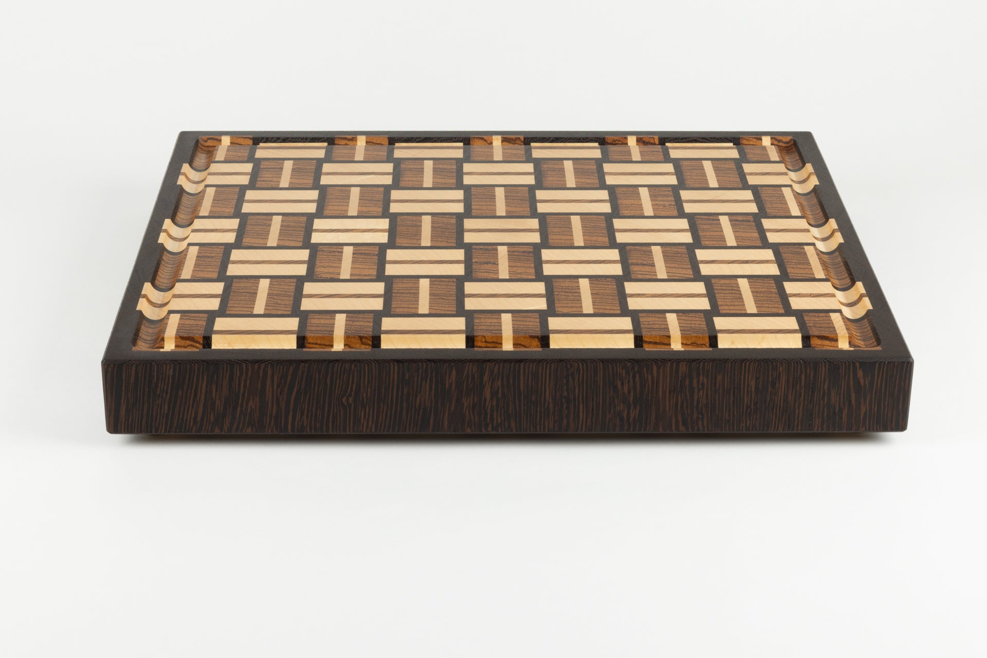 Planche à découper en bois de bout de luxe, modèle Berlioz. Vue de face mettant en valeur la bordure et le motif en damier tissé, essences nobles wengé, zebrano et érable, fabrication artisanale Made in France avec pieds en laiton massif.