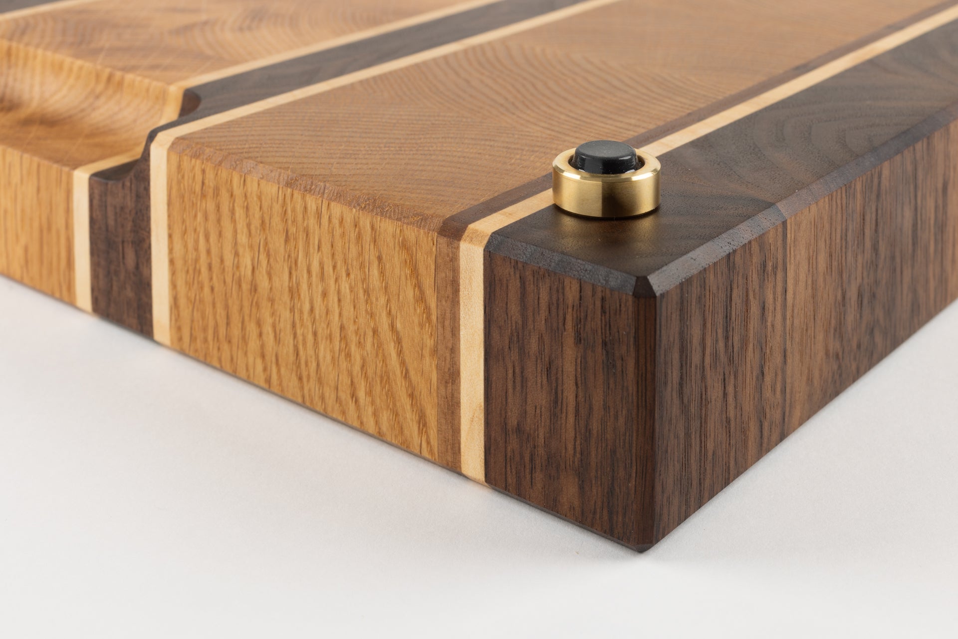 Vue du coin de la planche à découper en bois de bout artisanale Ravel, gros plan sur le pied en laiton massif Made in France avec patin antidérapant, essences de chêne français, noyer américain et érable, finitions haut de gamme.