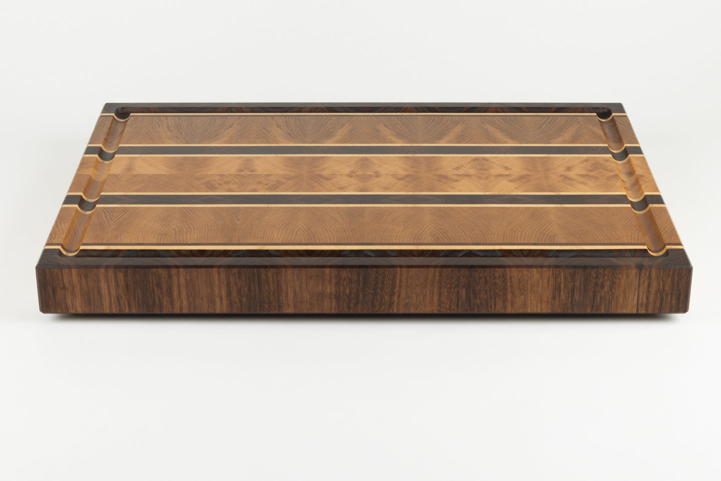 Planche à découper en bois de bout de luxe Ravel, vue frontale soulignant le veinage naturel du chêne français, du noyer américain et de l’érable, avec pieds en laiton massif et fabrication artisanale Made in France.