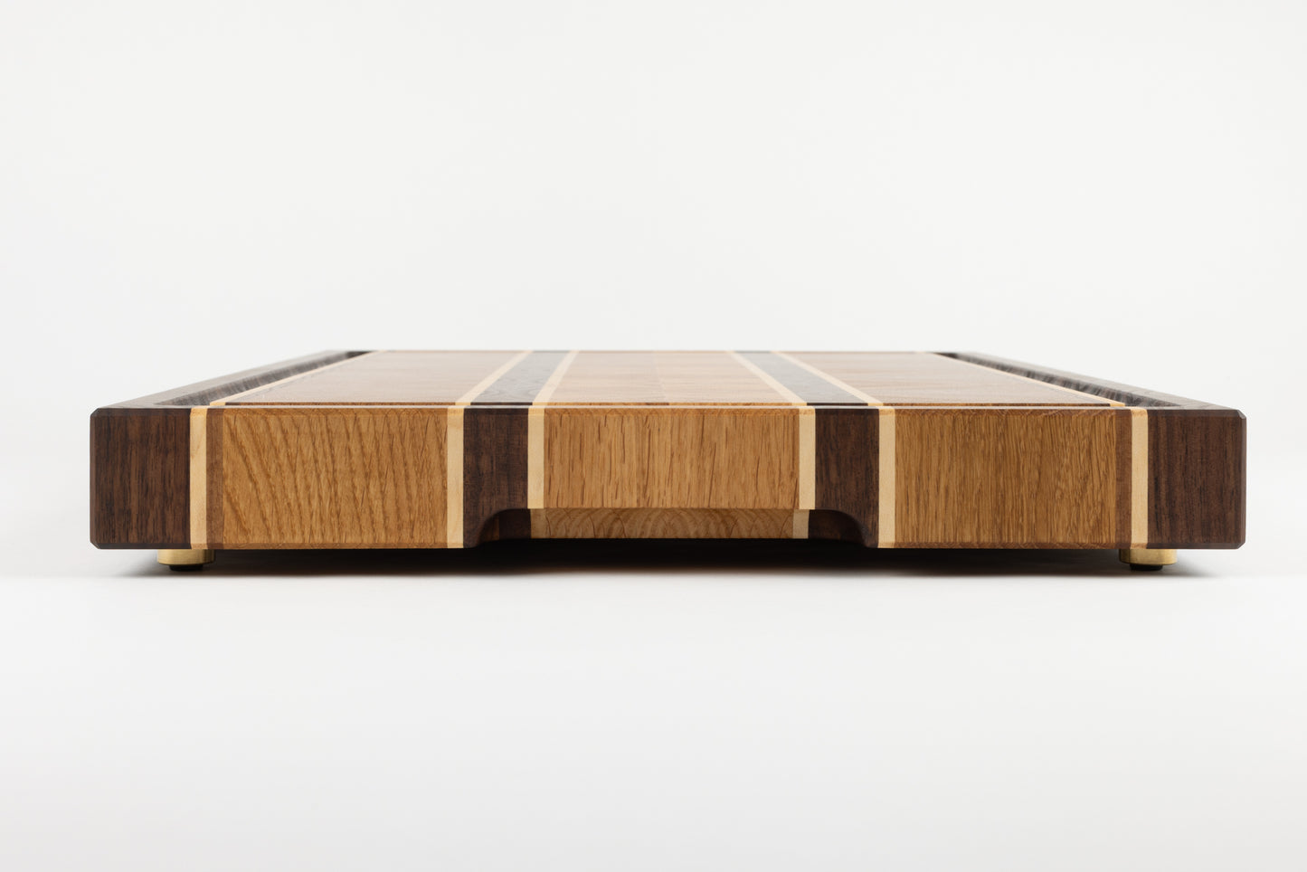 Planche à découper premium Ravel en bois de bout, vue latérale mettant en valeur la poignée fraisée et les pieds en laiton massif, chêne français, noyer américain et érable, finitions artisanales Made in France.