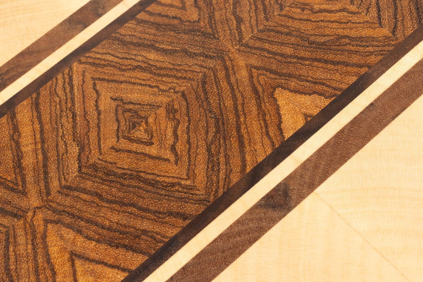 Gros plan sur l’assemblage central de la planche à découper Couperin, mettant en lumière le motif en miroir diamant du zebrano, encadré par de fines bandes d’érable et de noyer américain, fabrication artisanale en bois massif