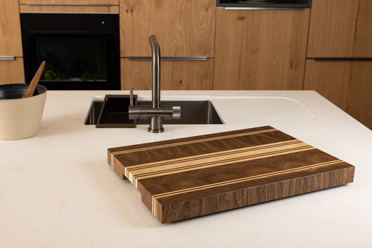 Planche à découper de luxe Debussy, en noyer français et érable, vue en situation dans une cuisine moderne en chêne, design élégant intemporel et fabrication Made in France haut de gamme.