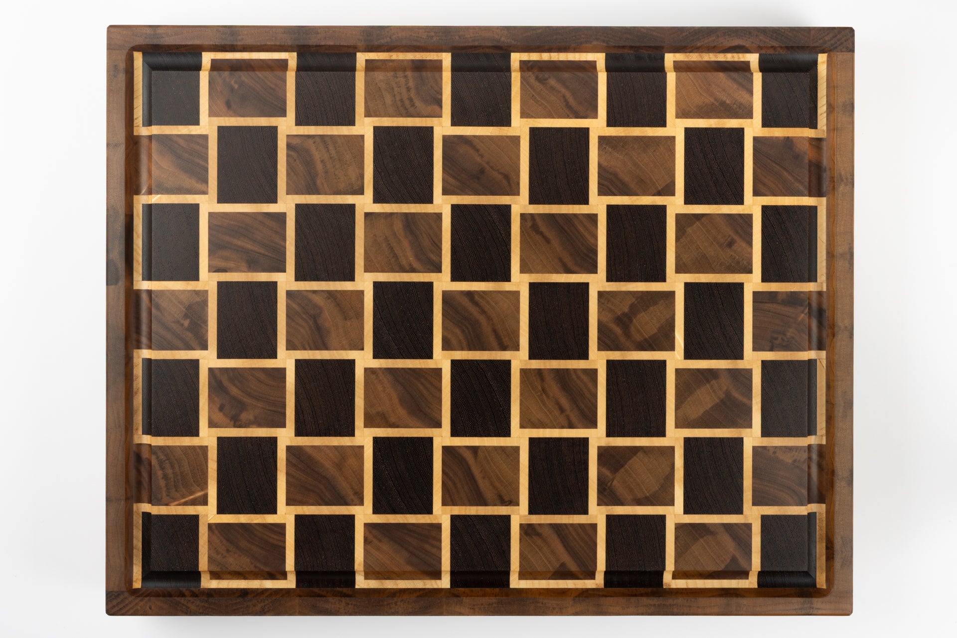 Planche à découper de luxe en bois massif, vue de dessus sur le motif damier tissé en noyer et érable, création artisanale Made in France.