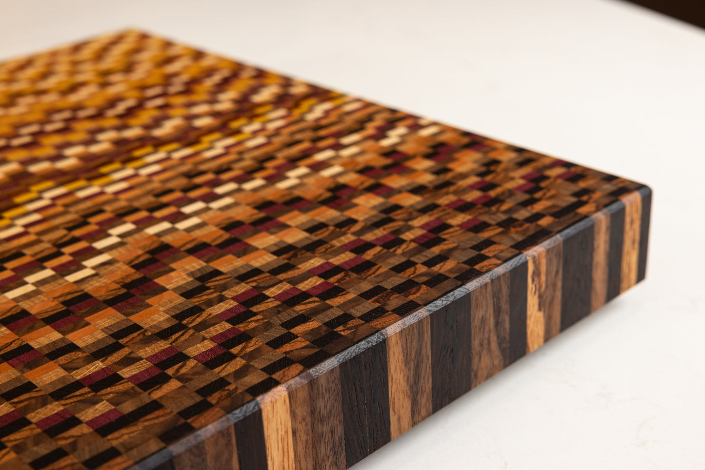 Vue sur la tranche et l'arrête soigneusement biseautée d’une planche à découper en bois de bout réalisée à partir de 11 essences de bois précieux.