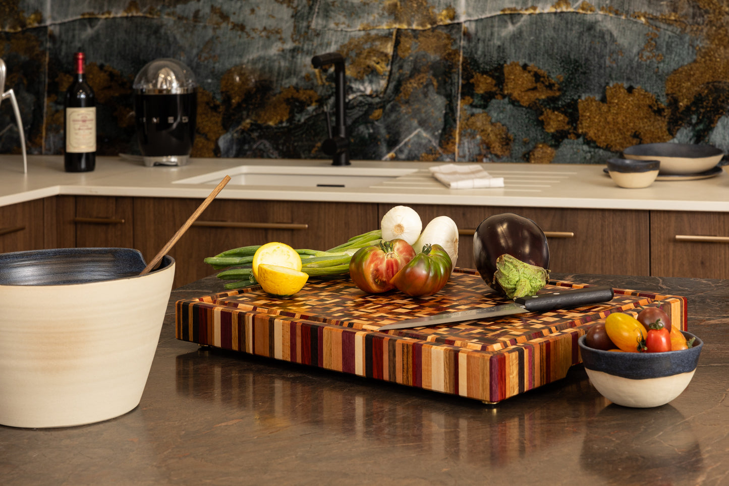 Vue générale de la planche à découper Messiaen en bois de bout précieux, sur plan de travail en granit. Mise en scène avec couteau de chef et légumes, fabrication artisanale française