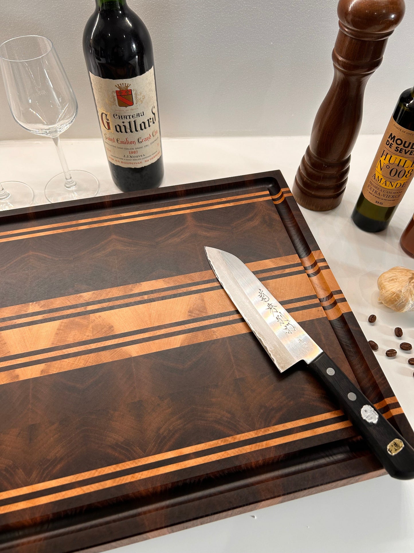 Planche à découper Debussy en bois de bout, réalisée en noyer et érable, en situation dans une cuisine avec un couteau et une bouteille de vin.