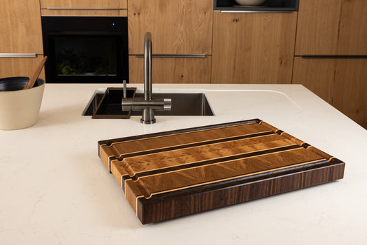 Vue de dessus de la planche à découper Ravel, en chêne, noyer et érable, soulignant le veinage contrasté et le design graphique du bois de bout. Pièce artisanale française haut de gamme, posée sur un plan de travail de cuisine moderne